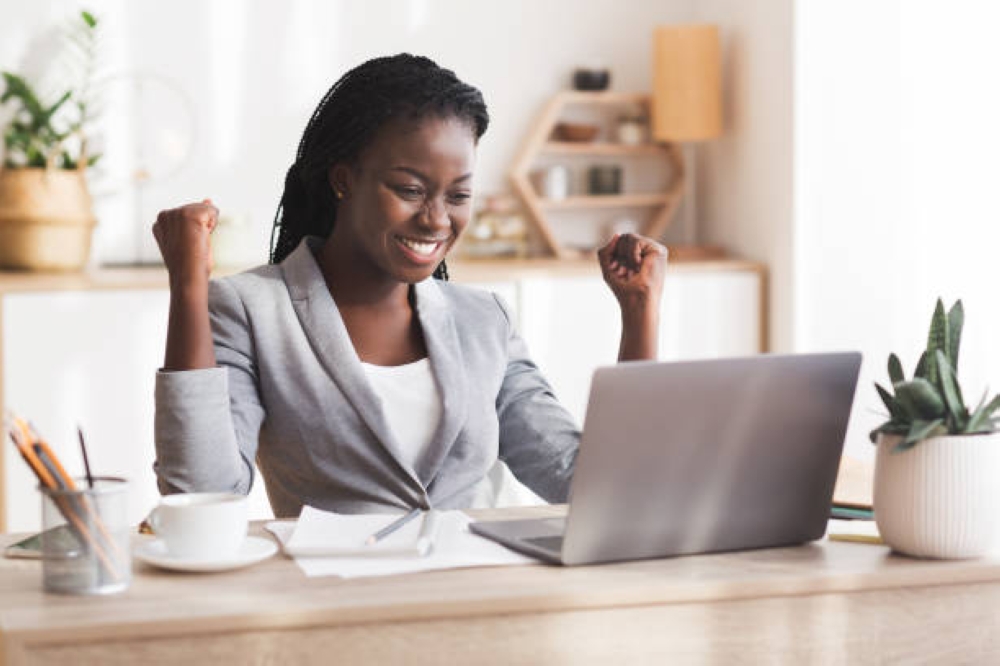 Excited African American Businesswoman Celebrating Success, Looking At Laptop Screen And Shaking Fists At Workplace In Modern Office, Free Space