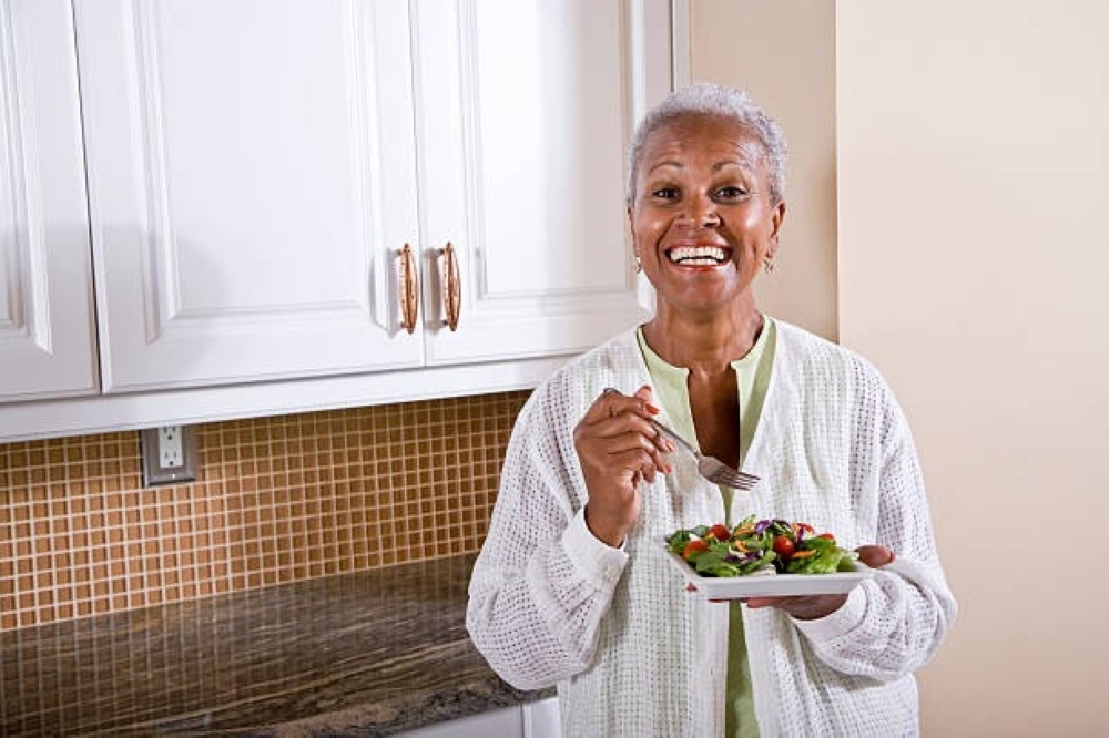 Mature African American woman eating healthy salad in kitchen