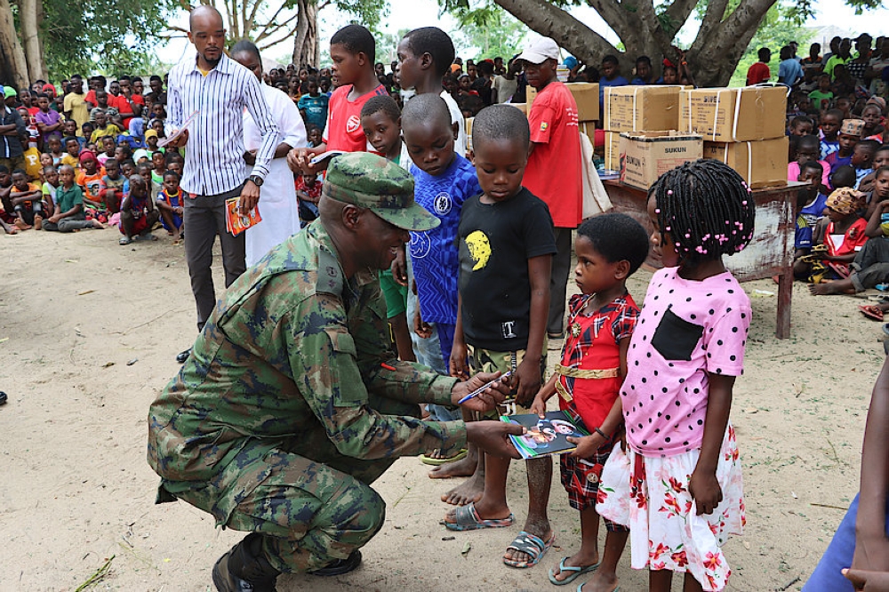Lt Col Guillaume Rutayisire, the Rwanda security forces (RSF) civil military cooperation officer, squats as he gives books to pupils at Escola Primaria Completa de Mute in Palma district, on Monday, February 13, 2023.

