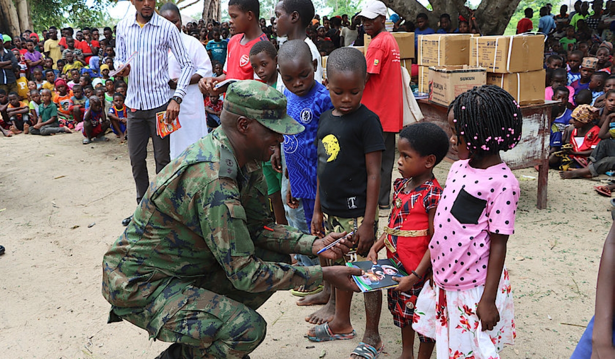 Lt Col Guillaume Rutayisire, the Rwanda security forces (RSF) civil military cooperation officer, squats as he gives books to pupils at Escola Primaria Completa de Mute in Palma district, on Monday, February 13, 2023.

