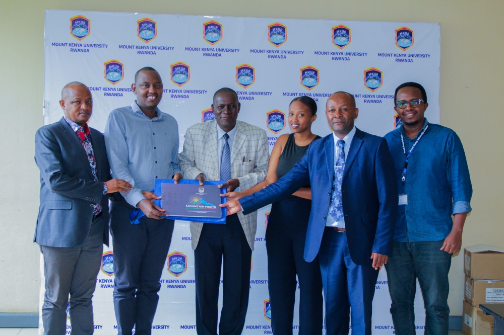 The Vice-Chancellor Designate, Prof Edwin Odhuno (3rd from left) hands over " Mountain Meets land of 1,000 hills" memoir to  Elijah Nyemina as members of staff of MKUR and a student, Mutoniwabo Benitha of School of Journalism and Mass Media looks on. Courtesy 