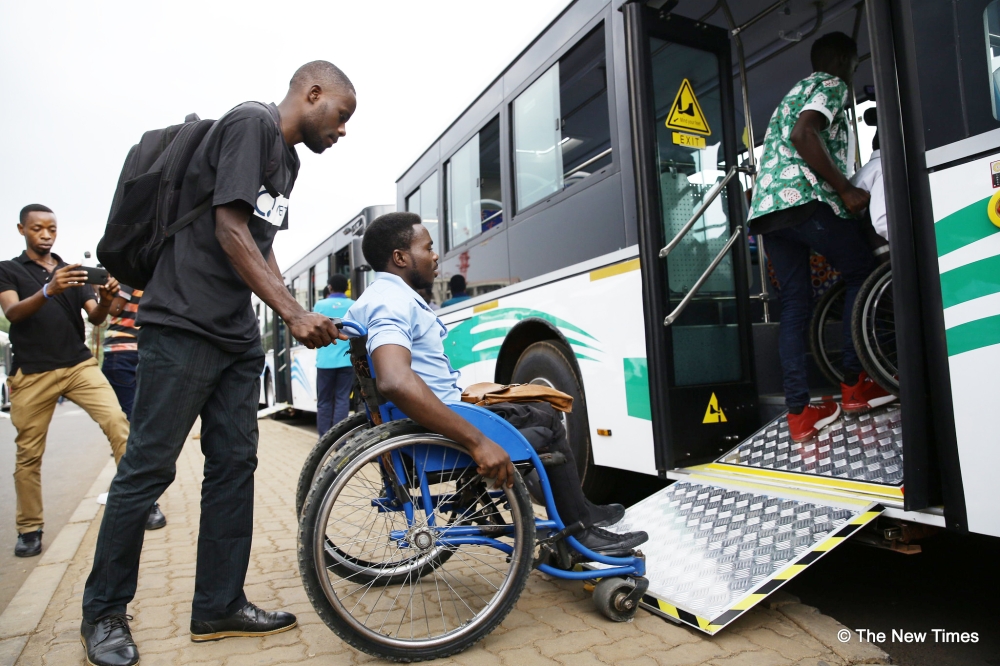 A caregiver assists a person with disability as he boards a bus at Kacyiru in Kigali Photo by Craish Bahizi