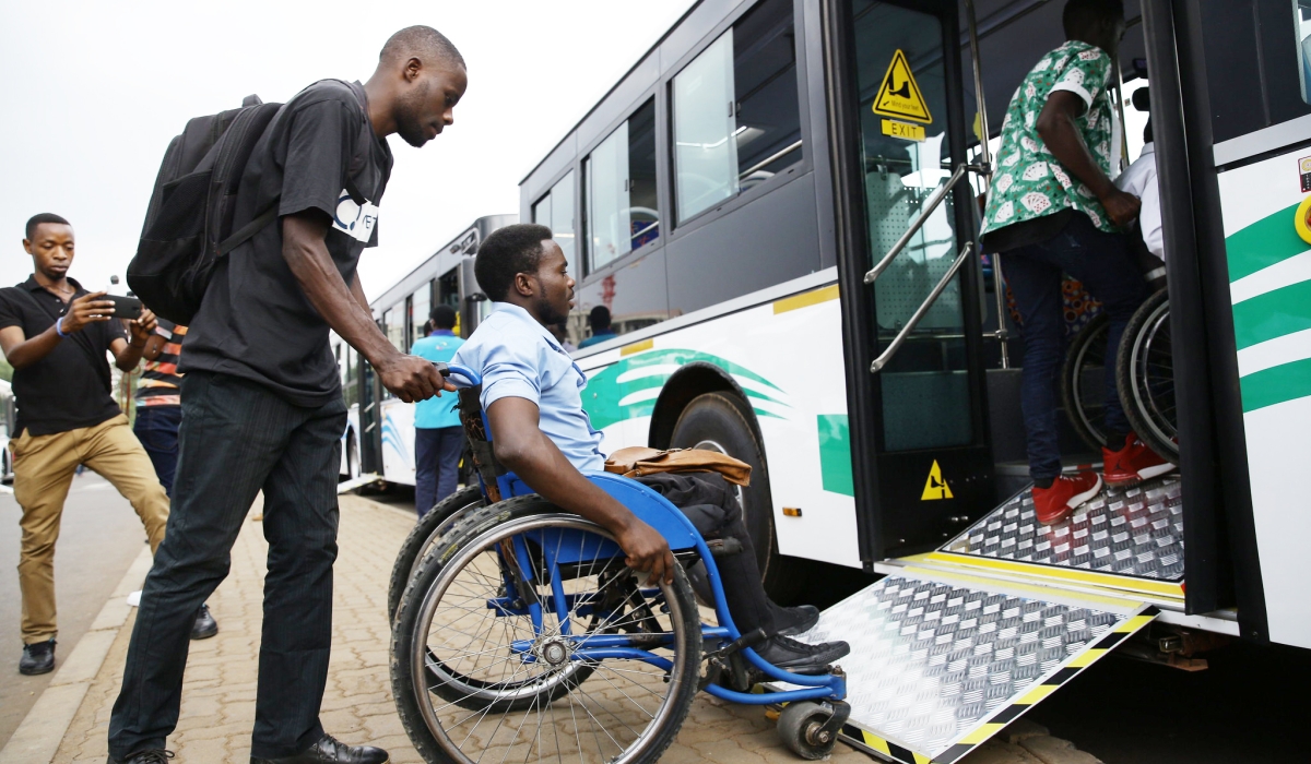 A caregiver assists a person with disability as he boards a bus at Kacyiru in Kigali Photo by Craish Bahizi