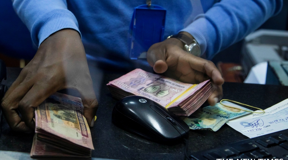 A bank teller counts money while serving customers at Bank of Kigali . File