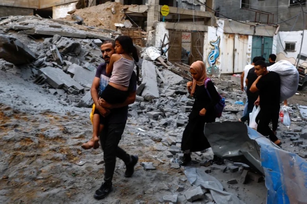Palestinians carry their belongings as they walk on a debris-strewn street in the aftermath of Israeli strikes in Gaza City [Mohammed Salem/Reuters]