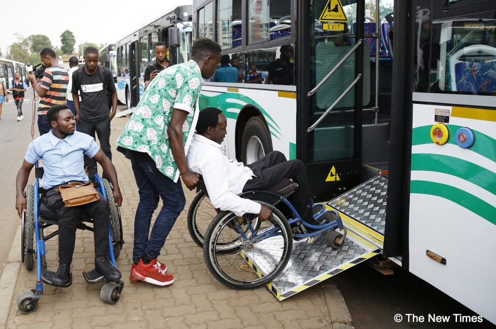 Two people with disabilities are assisted to board a bus in Kigali. Photo by Craish Bahizi