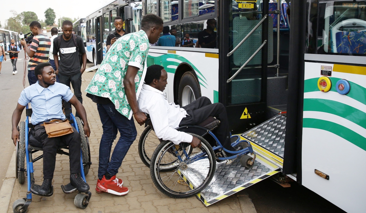 Two people with disabilities are assisted to board a bus in Kigali. Photo by Craish Bahizi