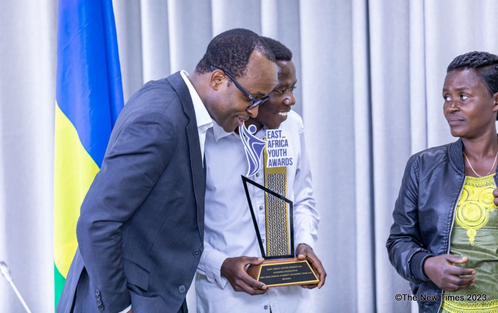 Minister of Education Gaspard Twagirayezu interacts with the 19-year-old,  Emile Cyubahiro who is the overall winner in sciences as his mother looks on during the event in Kigali on December 4. Photo by Dan Gatsinzi