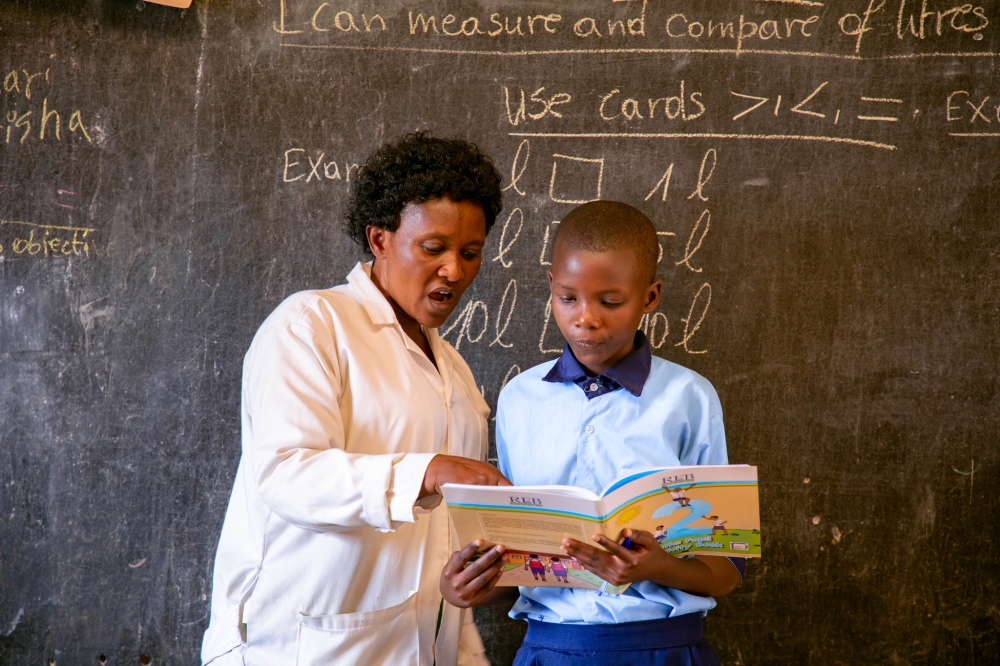 A teacher helps a child while reading a book at Ecole Primaire Kimisange.  Photo by Dan Gatsinzi