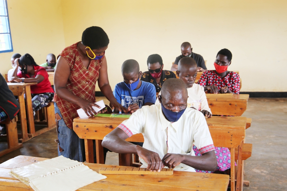 A teacher helps visually impaired people during a class for old people with disabilities at Masaka. Craish Bahizi