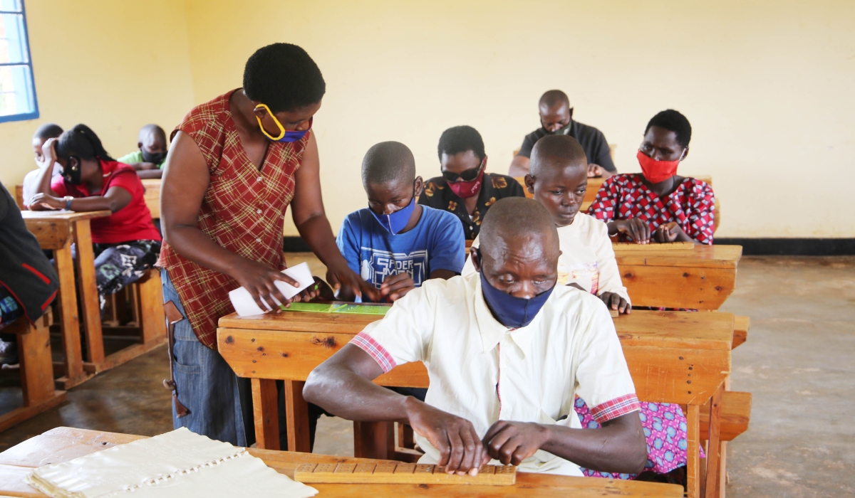 A teacher helps visually impaired people during a class for old people with disabilities at Masaka. Craish Bahizi