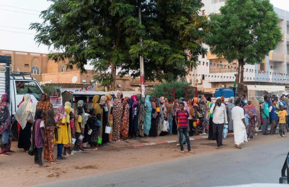 Recently displaced families queue for a food distribution alongside long-term residents in Omdurman, Sudan&#039;s second largest city.