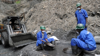 Workers at a mining site sift through mineral-rich soil using traditional panning techniques, as machinery operates nearby to support the extraction process. Courtesy 