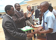 A primary school boy receives a Laptop from ICT Minister Romain Murenzi as primary and secondary school State Minister Mutsindashyaka looks on.(File photo)
