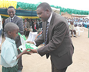 State Minister Theoneste Mutsindashyaka hands a laptop to a pupil as ICT  Minister Romain Murenzi looks on. (File Photo).