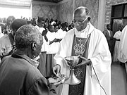 Retired Bishop  Fredrick Rubwijanga giving Holy Eucharist to Christians.