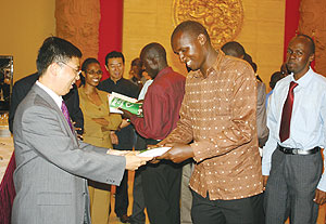 The Charge du2019Affaires at the Chinese embassy in Kigali, Li Yigang, hands over a text book to one of the students heading to China for further studies. (Photo/ F. Goodman)