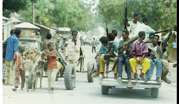 Children pulling a donkey cart watch a carload full of armed militiamen pass through the streets of Mogadishu