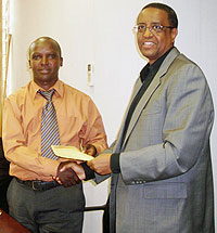 u2018One dollaru2019 campaign project manager Seyinzoga Nkongoli (L) receives a cheque from NUR Rector Prof Silas Lwakabamba. (Photo: P. Ntambara)