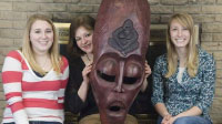 Simpson student Anna Ronnebaum, Professor Virginia Croskery and student Kayla Ferguson pose with a mask made by a Rwandan artisan. The three are part of a Simpson College group planning to travel to Rwanda in May. The mask was made for Simpson College dur