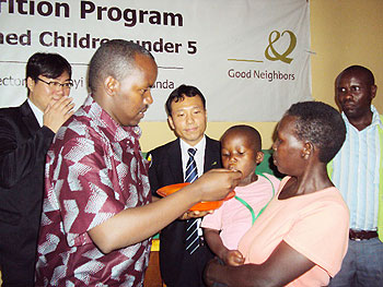 Kamonyi Mayor, Jacques Rutsinga, feeds a child as the Country Director of Good Neighbours,  Hong-Soo Chun, looks on, The New Times / Daniel Sabiiti.