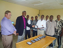 Bishop Laurent Mbanda hands over one of the Nooks hand set digital readers to students as Rwanda Leadership Foundation boss Gaylord Layton (L) looks on. The New Times / B. Mukombozi