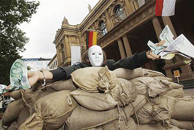 A protester holds fake money next to a wall of sandbags built during a protest against financial speculation in Frankfurt stock exchange June 17,2012. Net photo.
