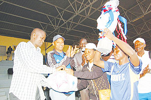 The Permanent Secretary in the Ministry of Sports and Culture, Edward Kalisa (L) hands over sports equipment to the captain of Vision Academy as Vision Youth Groupu2019s president John Bosco Birungi (R) looks on. Vision Academy lifted this yearu2019s EWSA and Ban
