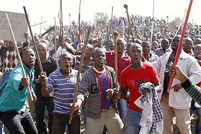 Striking mine workers sing as they hold weapons outside a South African mine in Rustenburg. Net photo.