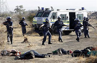 A policeman gestures in front of some of the dead miners after they were shot outside  a South African mine. Net photo.