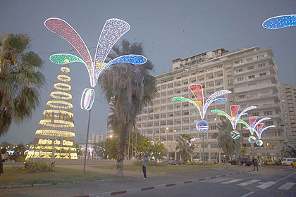 In this Tuesday, Dec. 11, 2012 photo, people walk past Christmas decorations in Independence Square in central Dakar, Senegal. As Christmas approaches in mostly Muslim Senegal, vendors ply the streets selling tinsel, artificial trees, and inflatable Santas, and the main boulevards are all aglow in holiday lights. 