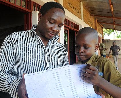 A curious Dodos Twiringiyimana from Good Harvest School accompanied by his father checks his marks at the school yesterday. The New Times, / John Mbanda.