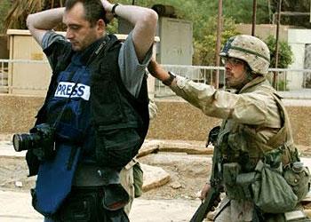 A soldier cross-examines a journalist in a conflict zone.