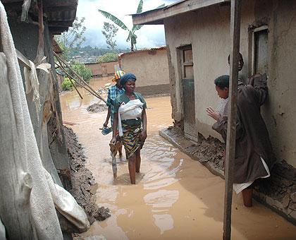Women wade through flood water in Rwaza last year. Residents evacuated from the area say they need more assistance. The New Times/ File.