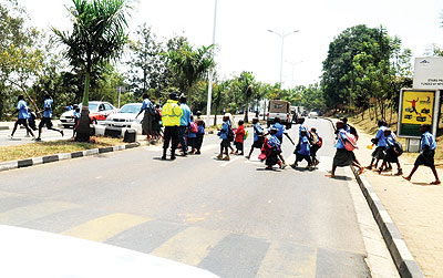 Traffic officers help school children to cross a busy road.  The New Times/ T. Kisambira.