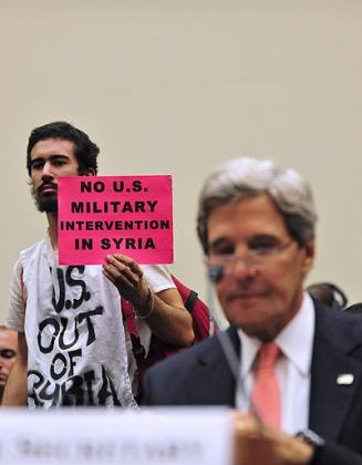A protester holds a banner as U.S. Secretary of State John Kerry testifies in a House of Representatives hearing about Syria on Capitol Hill in Washington Sept. 4, 2013.. Net photo.