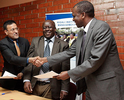 Fernandes (L) exchanges the MoU with Rutaremara as Pius Odunga, the Kim rector, looks on. The New Times/  John Mbanda.