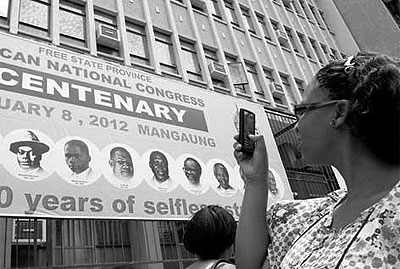 A woman photographs a poster in Bloemfontein that celebrates the centenary of South Africau2019s ruling party. The ANC expects 46 heads of state at its big birthday bash this weekend.  Net photo.