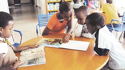 A volunteer helps children to read at the National Library in Kacyiru. Education Times/File Photo