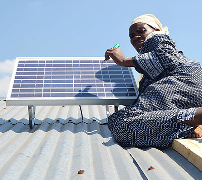 Mukamanzi fixes a solar panel atop a roof in Kinigi