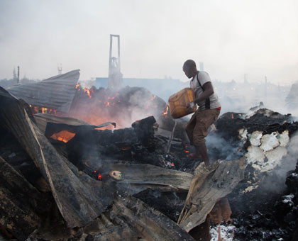 One of the residents who joined fire fighters in putting out the inferno that razed down a grain mill uses a jerrycan of water to put out smoldering fire yesterday. Timothy Kisambira.