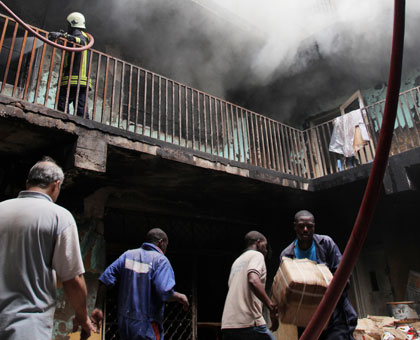 People remove property from the Muhima building as firefighters (top) battle the raging fires yesterday. John Mbanda.