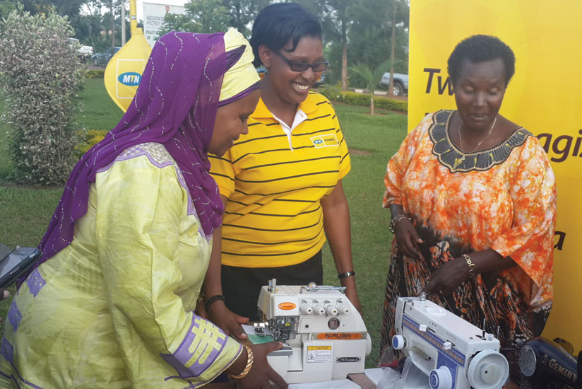 Mukarubega (left) is joined by Asiimwe to hand over some of the sewing machines to Nyiramanyana (right) at AVVAIS offices in Gahanga on Friday. (Donah Mbabazi)