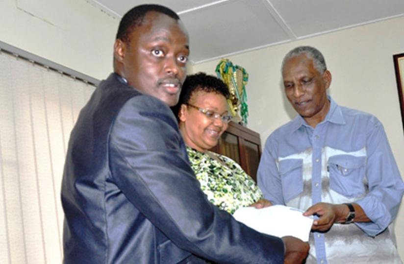 Kalisa (L) hands over the donation cheque to Sayinzoga as an unidentified woman looks on. (Courtesy)