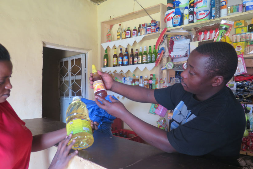 Ndayambaje helps a customers select cooking oil. The Kicukiro businessman runs a retail shops. (Dennis Agaba)