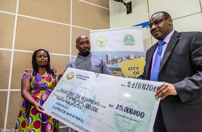 From L-R; City of Kigali staffers Challote Kayitesi and Jacques Masenga hand a dummy cheque to Finance minister Claver Gatete at the City head offices yesterday. (Timothy Kisambira)
