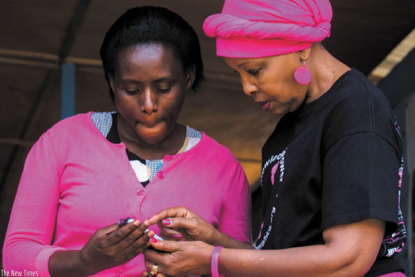 Kibugu (R) shows Mukarushema how the breast cancer awareness app works. (Timothy Kisambira)