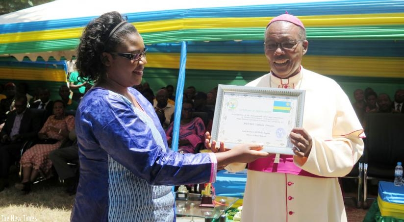 The Minister for Public Service and Labour, Judith Uwizeye, hands over an award of recognition by Huye District to the Bishop of Butare Catholic Diocese Monsignor Philip Rukamba on Tuesday. (Timothy Kisambira)