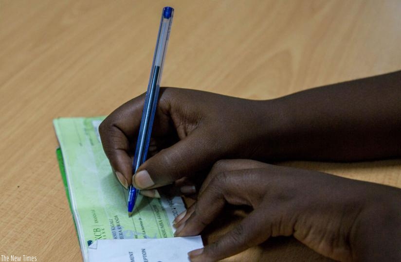 A bank client signs a cheque leaf. The central bank has instituted new punitive measures on persons who issue bounced cheques. (Doreen Umutesi)