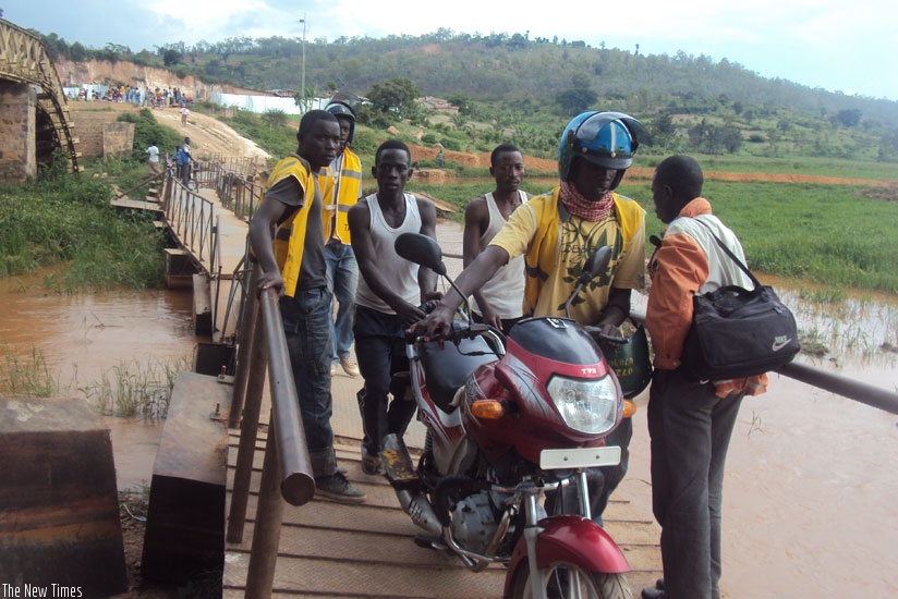 A motorcyclist being helped to cross Akanyaru River using a small bridge (right),  as the large bridge on the left is broken. (Courtesy)